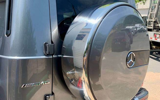 Comparison of dent on spare tire case attached behind backdoor of silver vehicle and repairs applied